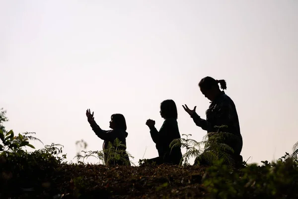 Silhouette of three woman kneeling down praying for worship God at white background. Christians pray to jesus christ for calmness. In morning people got to a quiet place and prayed. copy space.