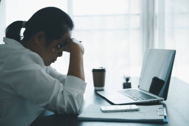 Yorgun ve stresli genç bayan çalışan kişi ofiste ahşap masa üzerinde çalışıyor. Profesyonel iş kadını uykulu, aşırı çalışmaktan bunalımda. Çalışan kadın iş yerinde endişeli hissediyor..