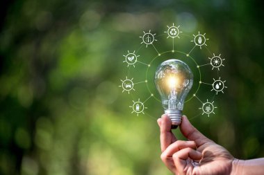 Yeşil yaprak üzerinde doğaya karşı el ele tutuşan ampul yenilenebilir ve sürdürülebilir enerji kaynakları ile birlikte. Enerji ve eko kavramından tasarruf.