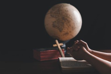 Hristiyan bir kadın dünya için dua ediyor ve dünyanın dört bir yanındaki insanlar İncil 'le ahşap masanın üzerinde. Hıristiyan eller ahşap bir masanın etrafında el ele dua ediyorlar..