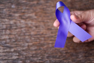 Koyu gri kırsal ahşap yüzeyde kadınlara uygulanan şiddetin kabul edilemez olduğunun farkındalığı için mor kurdele. Metin için boşluk olan üst görünüm. Aile içi şiddet farkındalığı.