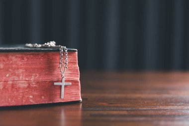 İncil 'in arka planında Hıristiyan haçı var. Ahşap Hıristiyan haçı gri masada bulanık ışıklara karşı, metin için boşluk.