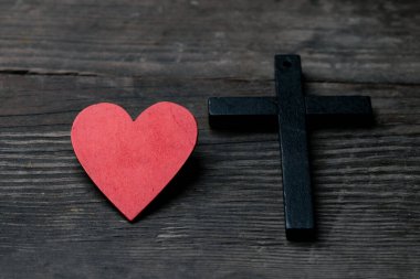 Siyah arka plandaki kırmızı kalp. Kalbin yanındaki haç da dahil. Haç Hristiyan dininin sembolüdür. Tanrı herkesi sever ve herkese yardım eder. Pazar dua etmek ve ibadet etmek için kiliseye git..