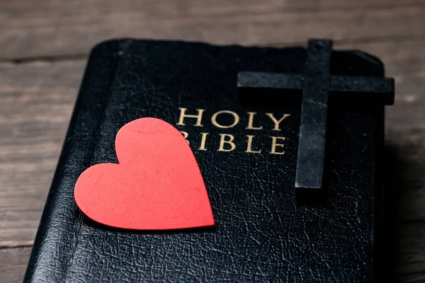 The red heart on holy bible book is the symbol of love from God. The God gives love to all people. We can see or find bible at the church. The bible is the in Christianity religion. Two heart on page.