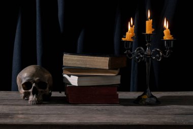 Mystical Candlelit Still Life with Skull ve Vintage Books for Halloween and Gothic Themes. Karanlık ve Atmosferik Durgun Yaşam: Makabre Düzenlemesindeki Kafatası, Mum ve Antika Kitaplar.