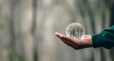 Human hands holding earth sphere crystal or sustainable globe glass with sunlight at green nature background in ecology environment forest. concept of conservation environmental, protection planet.