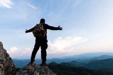 Kayalık dağın tepesinde erkek turist. Huzurlu bir adam yogada meditasyon yapıyor yalnız başına duruyor ve güneşin doğuşuyla birlikte bir dağın tepesinde kollarını açıyor..