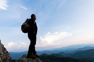 Kayalık dağın tepesinde erkek turist. Huzurlu bir adam yoga yapıyor, yalnız başına dinleniyor güneşin doğuşuyla birlikte bir dağın tepesinde duruyor..