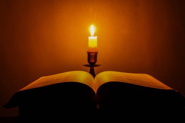 Candle with bible on a old oak wooden table. Beautiful gold background. Religion concept.