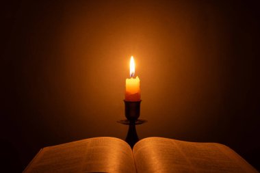 Candle with bible on a old oak wooden table. Beautiful gold background. Religion concept.