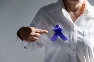 Gri arka planda mor kurdeleli kadın, mesaj için yeri olan yakın plan. Aile içi şiddet farkındalığı. Yaşayan insanları desteklemek için mor kurdele. Sağlık ve Dünya Kanser Günü konsepti.