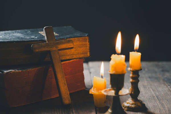 Зажгите свечу со священной библией и крестом или распятием на старом деревянном фоне в церкви. Свечи и открытая книга по изучению и чтению старинного деревянного стола христианства в домашних условиях.