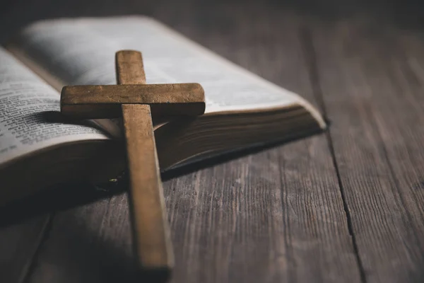 Light candle with holy bible and cross or crucifix on old wooden background in church.Candlelight and open book on vintage wood table christianity study and reading in home.Concept of christ religion