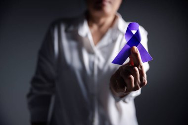 Gri arka planda mor kurdeleli kadın, mesaj için yeri olan yakın plan. Aile içi şiddet farkındalığı. Yaşayan insanları desteklemek için mor kurdele. Sağlık ve Dünya Kanser Günü konsepti.