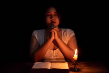 Gece karanlığında mum ışığında dua eden genç bir kız. Kadın kişi Tanrı 'ya inanç ve inançla tapar. Din, Hıristiyan dua kavramı. Hristiyan genç kız ve inanç.