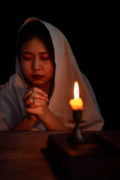 Young girl with candle light praying in dark night background. Woman person worship God with faith and belief. religion, christian prayer concept. Christian teenage girl and faith.