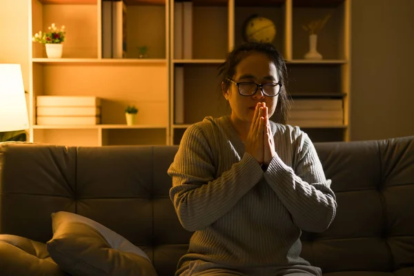 Christian religious woman praying at night sitting on couch in living dark room at home. Human person hands worship, Concept of praying to God. Female prayer with holy bible. Lady thanksgiving night