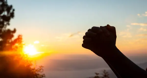 Silhouette of christian woman prayer on sunset background. Woman raising his hands in worship for peaceful life. Female praising God on the mountain. Christian religion concept.