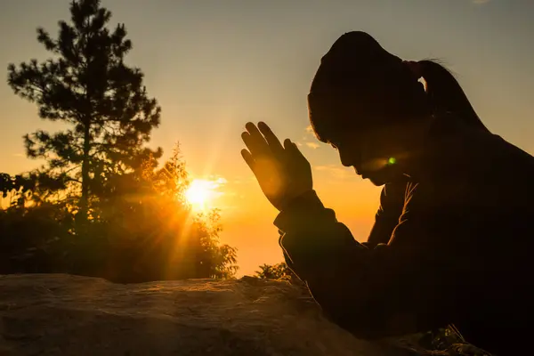 Woman kneeling to pray on Easter Day. Silhouette of prayer woman kneeling and praying over autumn sunset background. Forgive concept. praying over beautiful sunrise background
