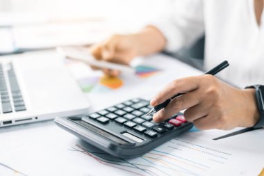 Finans işleriyle ilgilenen bir iş kadını ve ofis masraflarını hesaplayan bir masa. Muhasebe bankacılığı konsepti. Hesap makinesi ve mali muhasebe kullanan bir kadın..