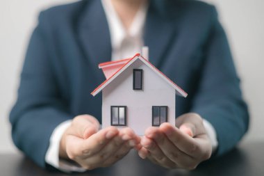 Ev sigortası konsepti. Ev sahibi, mülklerini sigorta acentesinin eline emanet etti. Evlerini ve maliyelerini ipotek sigortası planıyla güvence altına aldı..