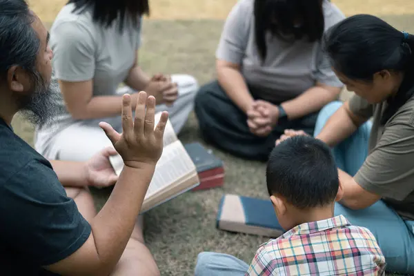 Young woman held her mother\'s hand in prayer, surrounded by their outdoor community, where love and family life flourished through shared moments of prayer and support. Group christian pray concept.