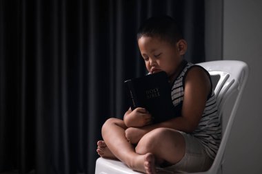 İnanç dolu küçük bir çocuk elinde kutsal İncil 'le oturup Tanrı' ya dua ediyor ve Hristiyan dinini kucaklıyor. çocuk, insan, İncil, çocuk, din, Hıristiyan, kutsal, küçük, inanç, Tanrı.