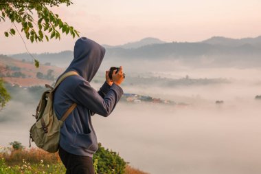 Gündoğumunda, tatilci, sis kaplı dağlarda yürüyüşün maceraperest yaşam tarzını benimsedi. Sırt çantası temel ihtiyaçlarla doluydu ve doğanın güzelliğine derin bir şükran duyuyordu. seyahat, gün doğumu, sis.