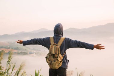 Gündoğumunda, tatilci, sis kaplı dağlarda yürüyüşün maceraperest yaşam tarzını benimsedi. Sırt çantası temel ihtiyaçlarla doluydu ve doğanın güzelliğine derin bir şükran duyuyordu. seyahat, gün doğumu, sis.