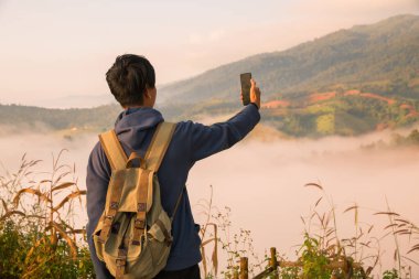 Gündoğumunda, tatilci, sis kaplı dağlarda yürüyüşün maceraperest yaşam tarzını benimsedi. Sırt çantası temel ihtiyaçlarla doluydu ve doğanın güzelliğine derin bir şükran duyuyordu. seyahat, gün doğumu, sis.