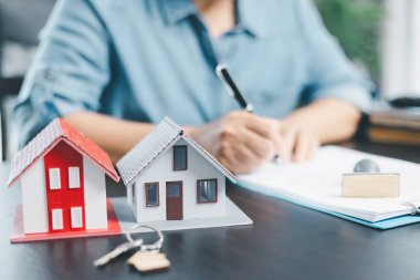 Kadın emlak komisyoncusu sunar ve model ev önerir, proje detaylarını ofiste oluşturur, satış başvurusu sözleşmesi imzalar, ipotek kredisi teklifiyle ilgili anlaşmalar ve sigorta.
