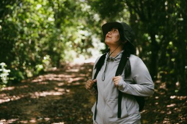 Sırt çantalı genç bir gezgin ulusal parkta ya da ormanda yürüyor. Doğada eğlence sporu. Kadın çantası, ormanda yürüyüş için el sallıyor. Ormanda macera. Sırt çantasıyla yürüyüş