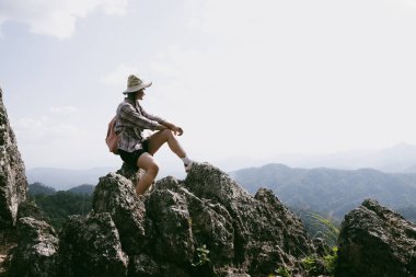 Dağın tepesinde kadın yürüyüşçü. Kolları dağın tepesinde gezen başarılı genç bir kadın zaferin tadını çıkarıyor. Gezgin dünyayı keşfediyor. Sırt çantalı yürüyüşçüler dinleniyor. Spor ve başarı konsepti.