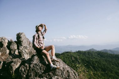Dağın tepesinde kadın yürüyüşçü. Kolları dağın tepesinde gezen başarılı genç bir kadın zaferin tadını çıkarıyor. Gezgin dünyayı keşfediyor. Sırt çantalı yürüyüşçüler dinleniyor. Spor ve başarı konsepti.