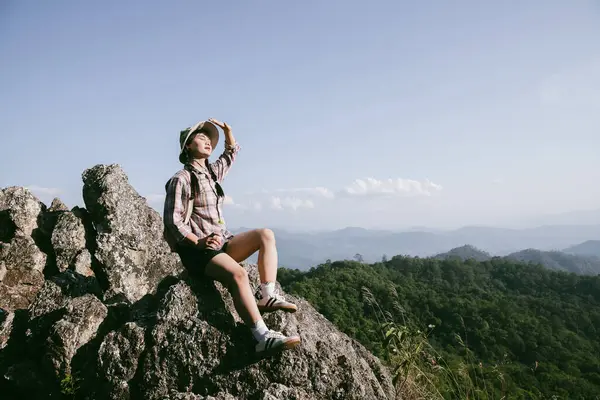 Dağın tepesinde kadın yürüyüşçü. Kolları dağın tepesinde gezen başarılı genç bir kadın zaferin tadını çıkarıyor. Gezgin dünyayı keşfediyor. Sırt çantalı yürüyüşçüler dinleniyor. Spor ve başarı konsepti.