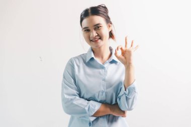 Asyalı bir kadın seviniyor, mutlu görünüyor, şampiyon, yumruk sallıyor, beyaz arka planda duruyor. Genç bir kadının yüzünde mutlu, pozitif bir ifade vardı. Parlak bir gülümsemeyle vurgulanmıştı..