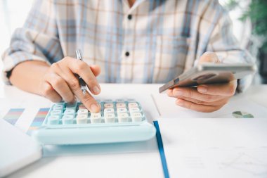 Ofisteki finans raporunu hesaplamak için hesap makinesi kullanan bir muhasebeci. işletme finansmanı, mali belgeleri düzenleyerek vergi hesaplama, gelir yatırımlarını takip etme, elle hesaplama.