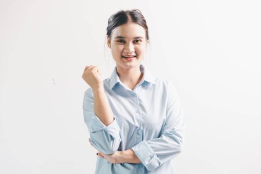 Asyalı bir kadın seviniyor, mutlu görünüyor, şampiyon, yumruk sallıyor, beyaz arka planda duruyor. Genç bir kadının yüzünde mutlu, pozitif bir ifade vardı. Parlak bir gülümsemeyle vurgulanmıştı..