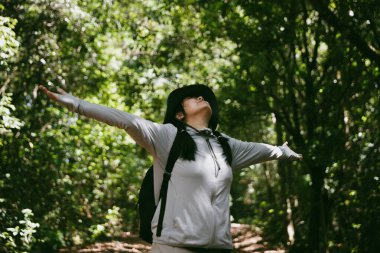 Sırt çantalı genç bir gezgin ulusal parkta ya da ormanda yürüyor. Doğada eğlence sporu. Kadın çantası, ormanda yürüyüş için el sallıyor. Ormanda macera. Sırt çantasıyla yürüyüş