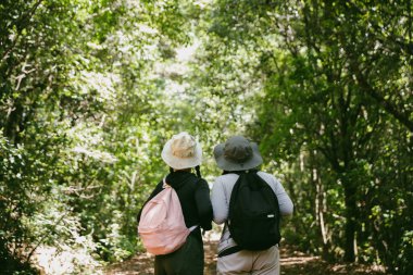 Sırt çantalı iki bayan arkadaş birlikte kırda yürüyüş yapıyorlar. Asyalı arkadaş kız sırt çantalı arkadaş ormanda birlikte seyahat eder. Yürüyüş yaparken mutlu ve güneşli bir gün..