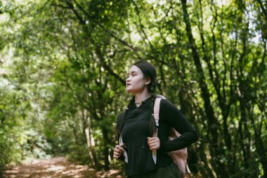 Sırt çantalı genç bir gezgin ulusal parkta ya da ormanda yürüyor. Doğada eğlence sporu. Kadın çantası, ormanda yürüyüş için el sallıyor. Ormanda macera. Sırt çantasıyla yürüyüş