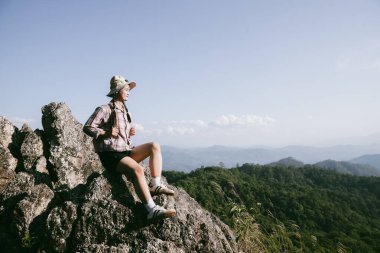 Dağın tepesinde kadın yürüyüşçü. Kolları dağın tepesinde gezen başarılı genç bir kadın zaferin tadını çıkarıyor. Gezgin dünyayı keşfediyor. Sırt çantalı yürüyüşçüler dinleniyor. Spor ve başarı konsepti.