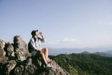 Dağın tepesinde kadın yürüyüşçü. Kolları dağın tepesinde gezen başarılı genç bir kadın zaferin tadını çıkarıyor. Gezgin dünyayı keşfediyor. Sırt çantalı yürüyüşçüler dinleniyor. Spor ve başarı konsepti.