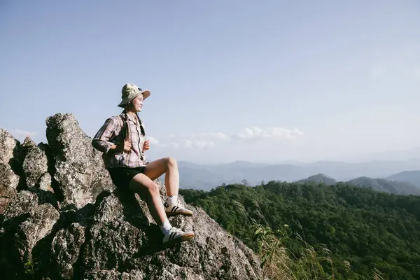 Dağın tepesinde kadın yürüyüşçü. Kolları dağın tepesinde gezen başarılı genç bir kadın zaferin tadını çıkarıyor. Gezgin dünyayı keşfediyor. Sırt çantalı yürüyüşçüler dinleniyor. Spor ve başarı konsepti.