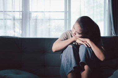 Depresyondaki kadın kanepeye oturur. Kederli insan yalnız başına oturur ve dizlerine sarılır sıkıcı üzgün üzgün sinirli sinirli. Boğucu bir yük altında umut bulmak için mücadele ediyorlar. ruh sağlığı kavramı.