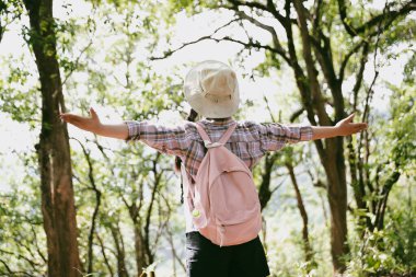 Sırt çantalı genç bir gezgin ulusal parkta ya da ormanda yürüyor. Doğada eğlence sporu. Kadın çantası, ormanda yürüyüş için el sallıyor. Ormanda macera. Sırt çantasıyla yürüyüş