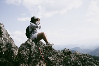 Dağın tepesinde kadın yürüyüşçü. Kolları dağın tepesinde gezen başarılı genç bir kadın zaferin tadını çıkarıyor. Gezgin dünyayı keşfediyor. Sırt çantalı yürüyüşçüler dinleniyor. Spor ve başarı konsepti.