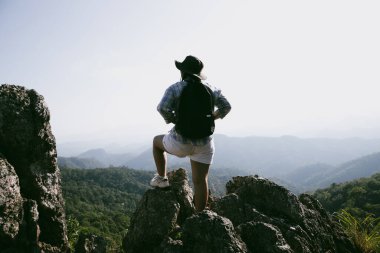 Dağın tepesinde kadın yürüyüşçü. Kolları dağın tepesinde gezen başarılı genç bir kadın zaferin tadını çıkarıyor. Gezgin dünyayı keşfediyor. Sırt çantalı yürüyüşçüler dinleniyor. Spor ve başarı konsepti.