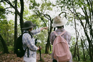 Sırt çantalı iki bayan arkadaş birlikte kırda yürüyüş yapıyorlar. Asyalı arkadaş kız sırt çantalı arkadaş ormanda birlikte seyahat eder. Yürüyüş yaparken mutlu ve güneşli bir gün..
