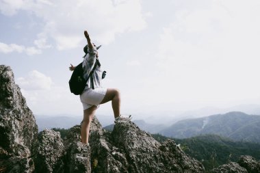 Dağın tepesinde kadın yürüyüşçü. Kolları dağın tepesinde gezen başarılı genç bir kadın zaferin tadını çıkarıyor. Gezgin dünyayı keşfediyor. Sırt çantalı yürüyüşçüler dinleniyor. Spor ve başarı konsepti.